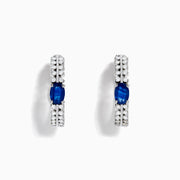 The 14K White Gold Blue Sapphire and Diamond Hoops feature an oval blue sapphire at the center, accented by rows of sparkling diamonds. Displayed on a plain white background.