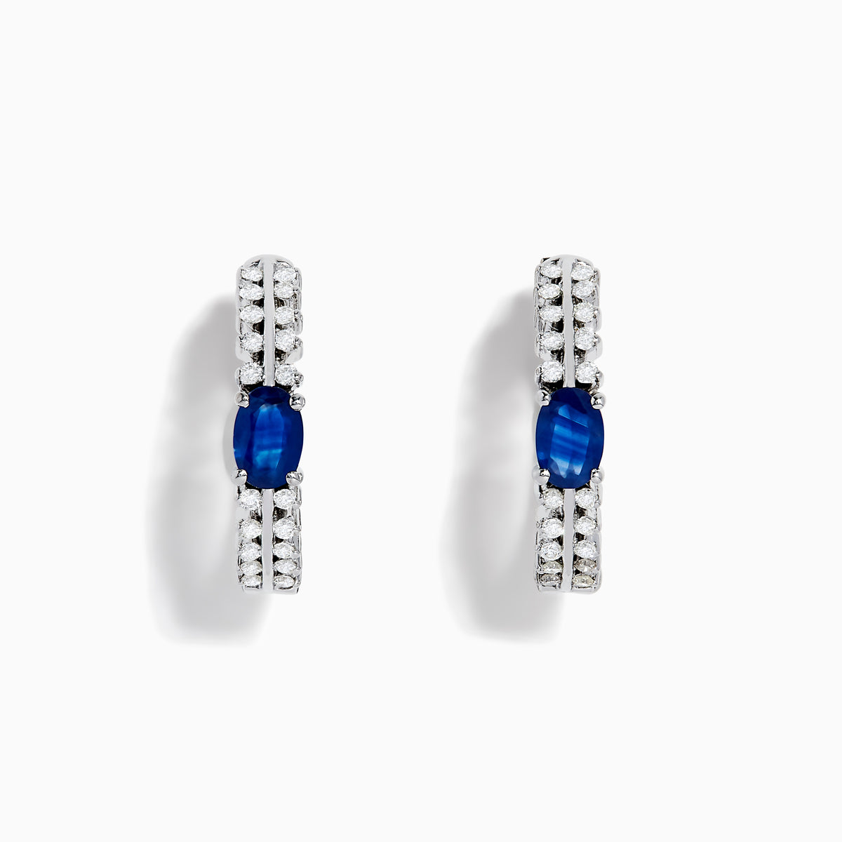The 14K White Gold Blue Sapphire and Diamond Hoops feature an oval blue sapphire at the center, accented by rows of sparkling diamonds. Displayed on a plain white background.
