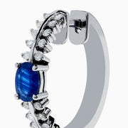 The 14K White Gold Blue Sapphire and Diamond Hoops feature an oval blue sapphire at the center, accented by rows of sparkling diamonds. Displayed on a plain white background.
