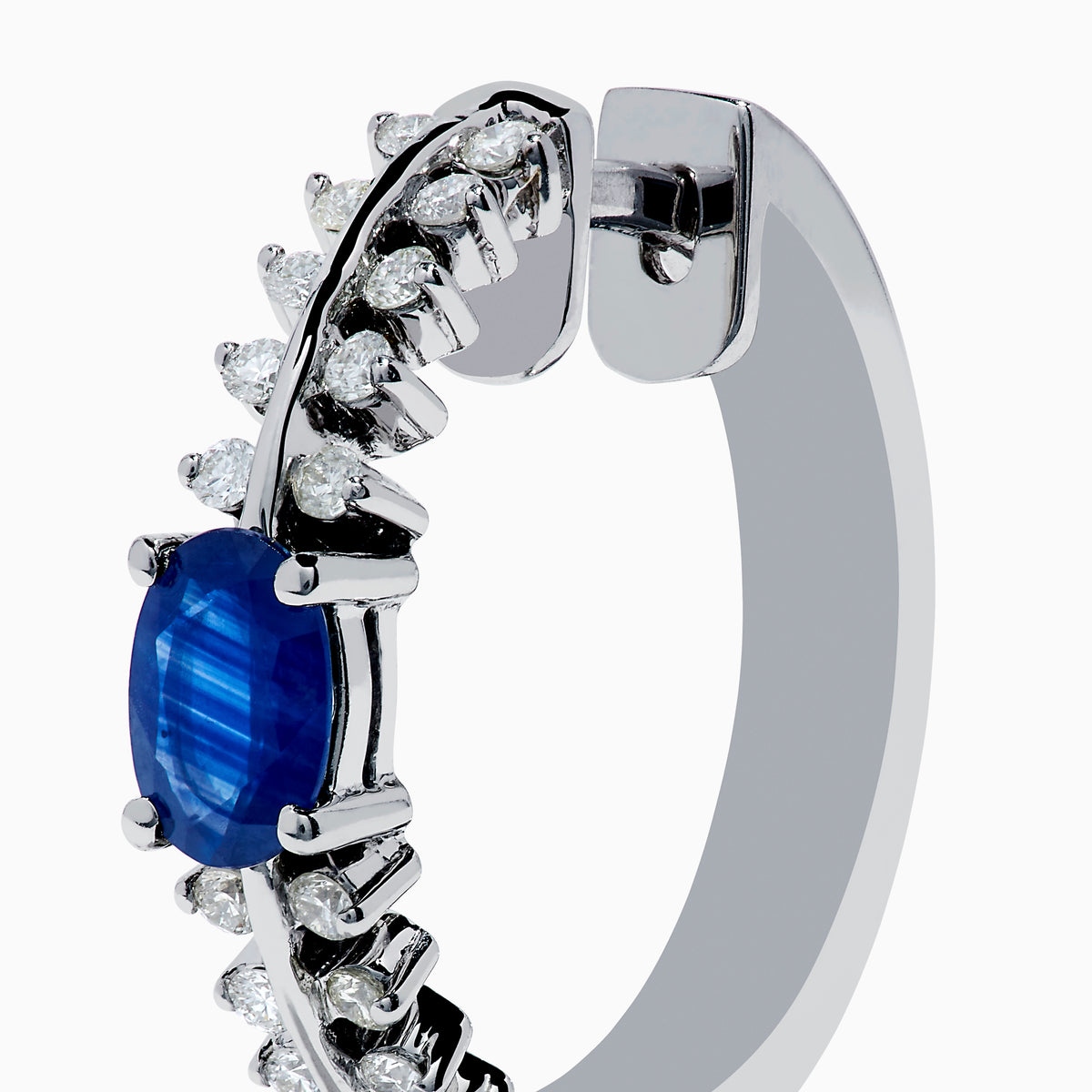 The 14K White Gold Blue Sapphire and Diamond Hoops feature an oval blue sapphire at the center, accented by rows of sparkling diamonds. Displayed on a plain white background.