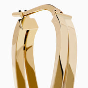The 14K Yellow Gold Double Bar Hoops feature a shiny, modern twisted design with intertwined double bars, shown on a white background.