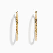 A pair of 14K Yellow Gold Crystal Cut Tube Hoops, large and textured, are displayed vertically on a white background with soft shadows beneath each earring.