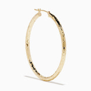 A pair of 14K Yellow Gold Crystal Cut Tube Hoops, large and textured, are displayed vertically on a white background with soft shadows beneath each earring.