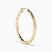 A pair of 14K Yellow Gold Chevron Cut Tube Hoops, displayed against a white background with soft shadows.
