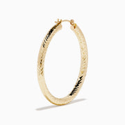 A pair of 14K Yellow Gold Chevron Cut Tube Hoops, displayed against a white background with soft shadows.