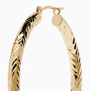 A pair of 14K Yellow Gold Chevron Cut Tube Hoops, displayed against a white background with soft shadows.
