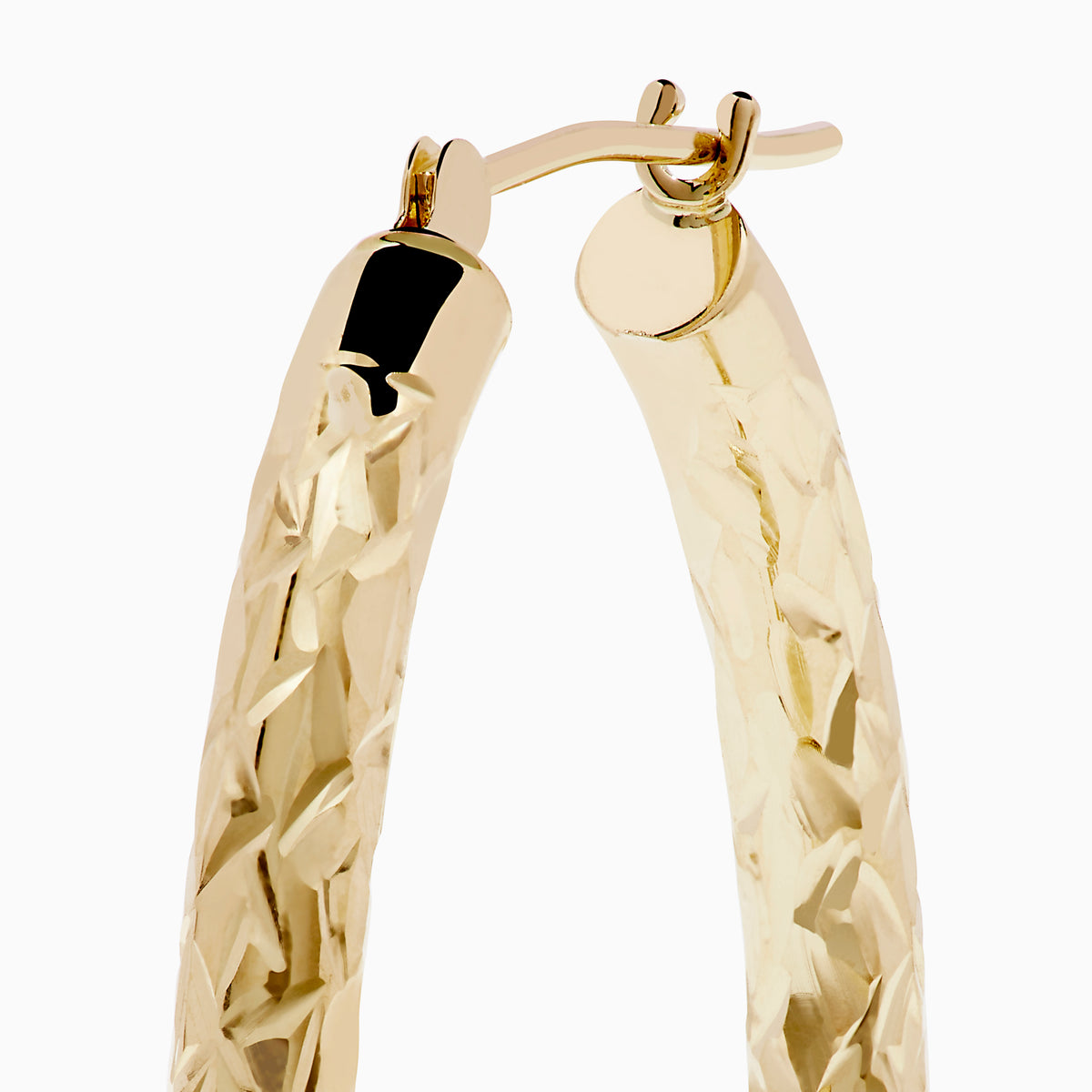 The 14K Yellow Gold Crystal Cut Tube Oval Hoops feature a textured, engraved floral pattern and delicate crystal cut detailing, shown against a plain white background.