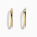 A pair of 14K Yellow Gold Hollow Oval Hoop Earrings displayed vertically on a white background, casting soft shadows to the right.