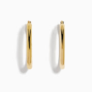 A pair of 14K Yellow Gold Hollow Oval Hoop Earrings displayed vertically on a white background, casting soft shadows to the right.