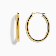 A pair of 14K Yellow Gold Hollow Oval Hoop Earrings displayed vertically on a white background, casting soft shadows to the right.
