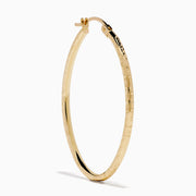 A pair of 14K Yellow Gold Oval Tube Baguette Cut Hoop Earrings, thin and textured, are displayed vertically with clasps at the top against a plain white background.