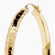 The 14K Yellow Gold Reverse Vibrant Cut Hoop Earrings feature a large, eye-catching design and are showcased against a plain white background with soft shadows.