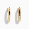 The 14K Yellow Gold Tube Hoop Earrings are shown vertically on a plain white background, with soft shadows cast to the left.