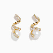 The 14K Yellow Gold Fresh Water Pearl and Diamond Ribbon Earrings feature a spiral gold design encrusted with small diamonds, elegantly encircling a large freshwater pearl, all showcased on a plain white background.