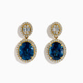 The 14K Yellow Gold Blue Topaz and Diamond Oval Drop Earrings feature large oval blue topaz gemstones encircled by white diamonds, with a sparkling diamond cluster above each stone for an elegant drop design.