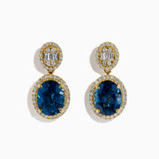 The 14K Yellow Gold Blue Topaz and Diamond Oval Drop Earrings feature large oval blue topaz gemstones encircled by white diamonds, with a sparkling diamond cluster above each stone for an elegant drop design.