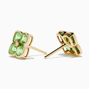 The 14K Yellow Gold Peridot and Diamond Earrings are four-petal flower studs featuring peridot gemstones on each petal with a central diamond, displayed against a white background.