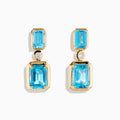 Elegant and symmetrical, the 14K Yellow Gold Blue Topaz and Diamond Drop Earrings display rectangular blue topaz stones with smaller gems above, separated by a sparkling diamond drop, set against a white background.