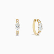 Lab Grown Diamond Marquise Huggie Earrings in 14K Yellow Gold, each showcasing a central round diamond and smaller accent diamonds along the vertical sides, displayed on a plain white background.