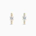 The Lab Grown Diamond Round Huggie Earrings in 14K Yellow Gold feature a central round lab diamond accented by a row of smaller lab diamonds, all set in sleek yellow gold and displayed on a white background.