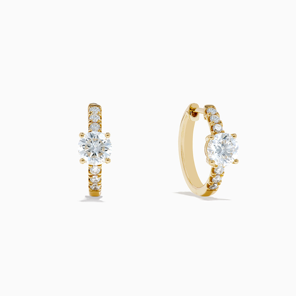 The Lab Grown Diamond Round Huggie Earrings in 14K Yellow Gold feature a central round lab diamond accented by a row of smaller lab diamonds, all set in sleek yellow gold and displayed on a white background.