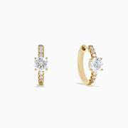The Lab Grown Diamond Round Huggie Earrings in 14K Yellow Gold feature a central round lab diamond accented by a row of smaller lab diamonds, all set in sleek yellow gold and displayed on a white background.
