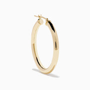 The 14K Yellow Gold Hollow Tube Hoops are sleek, polished earrings shown side by side against a white background, featuring classic yellow gold in a timeless hoop design with clasps at the top.