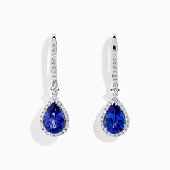 The Nahla 14K White Gold Tanzanite and Diamond Dangle Halo Earrings feature teardrop-shaped tanzanite stones surrounded by sparkling diamonds, set in elegant white gold and displayed against a white background.