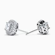 The 18K White Gold Diamond Double Halo Cushion Stud Earrings feature cushion-cut diamonds surrounded by double halos of smaller diamonds, set in 18K white gold and displayed on a white background.