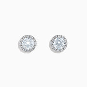 A pair of 14K White Gold Lab Grown Diamond Earrings with a central round diamond and a halo of smaller lab grown diamonds, set against a white background.