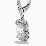 The Lab Grown Diamond Emerald Cut Dangle Earrings in 14K White Gold showcase emerald cut lab grown centers with a halo of round diamonds and diamond-encrusted hooks, elegantly presented against a white background.