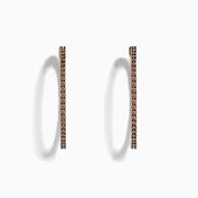 The 14K Rose Gold Brown Diamond 1.5 Inch Hoop Earrings, featuring slim vertical hoops with dark brown diamonds, are photographed against a plain white background, casting soft oval-shaped shadows to the left.