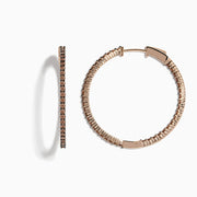 The 14K Rose Gold Brown Diamond 1.5 Inch Hoop Earrings, featuring slim vertical hoops with dark brown diamonds, are photographed against a plain white background, casting soft oval-shaped shadows to the left.