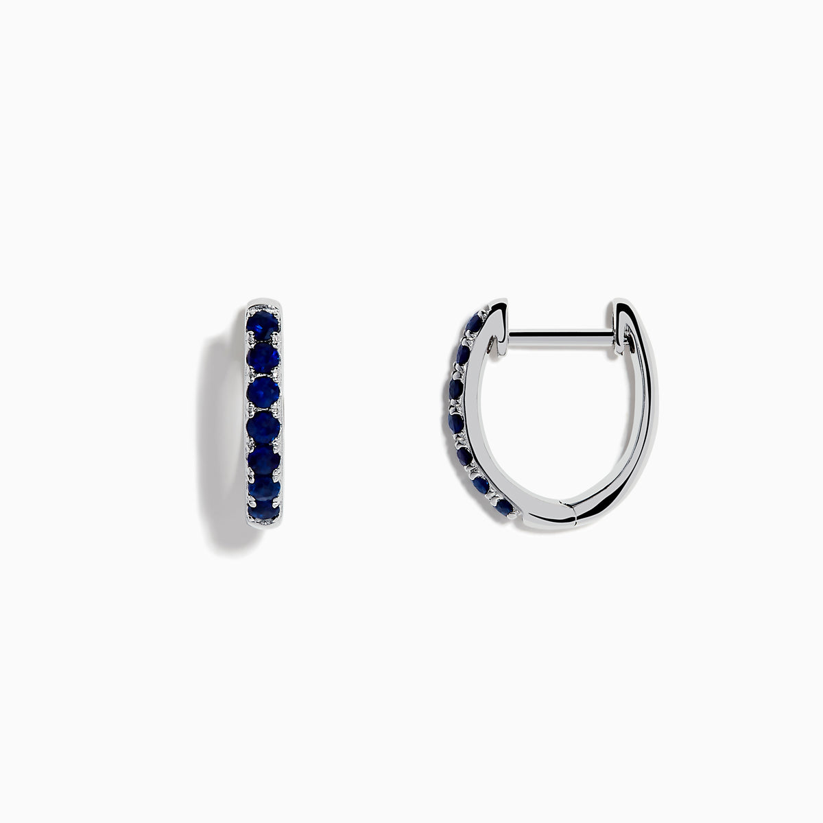 The Royale Bleu 14 Karat White Gold Blue Sapphire Huggie Hoop Earrings feature a row of round, dark blue sapphires and are shown against a plain white background.