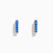The Royale Bleu 14K White Gold Sapphire Huggie Earrings feature a row of round blue sapphires and are displayed against a white background.