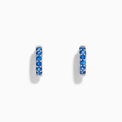 The Royale Bleu 14K White Gold Sapphire Huggie Earrings feature a row of round blue sapphires and are displayed against a white background.