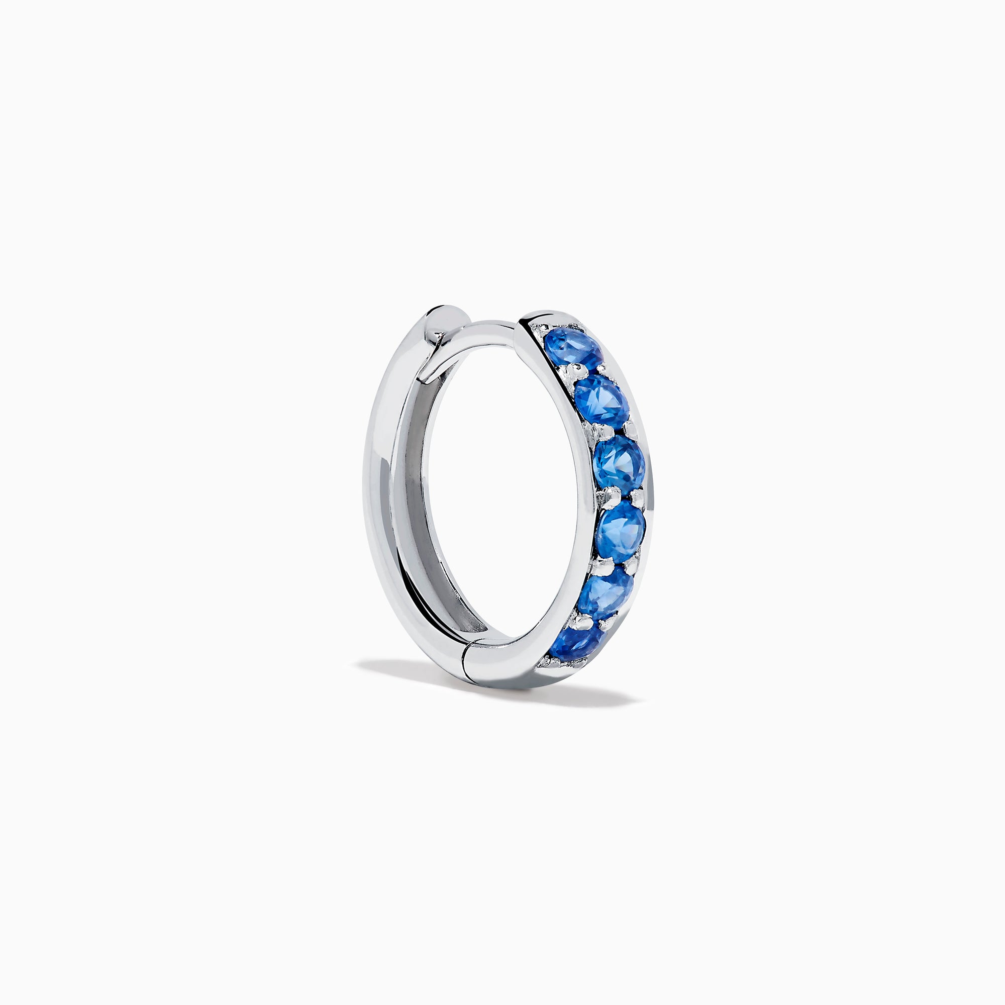 The Royale Bleu 14K White Gold Sapphire Huggie Earrings feature a row of round blue sapphires and are displayed against a white background.