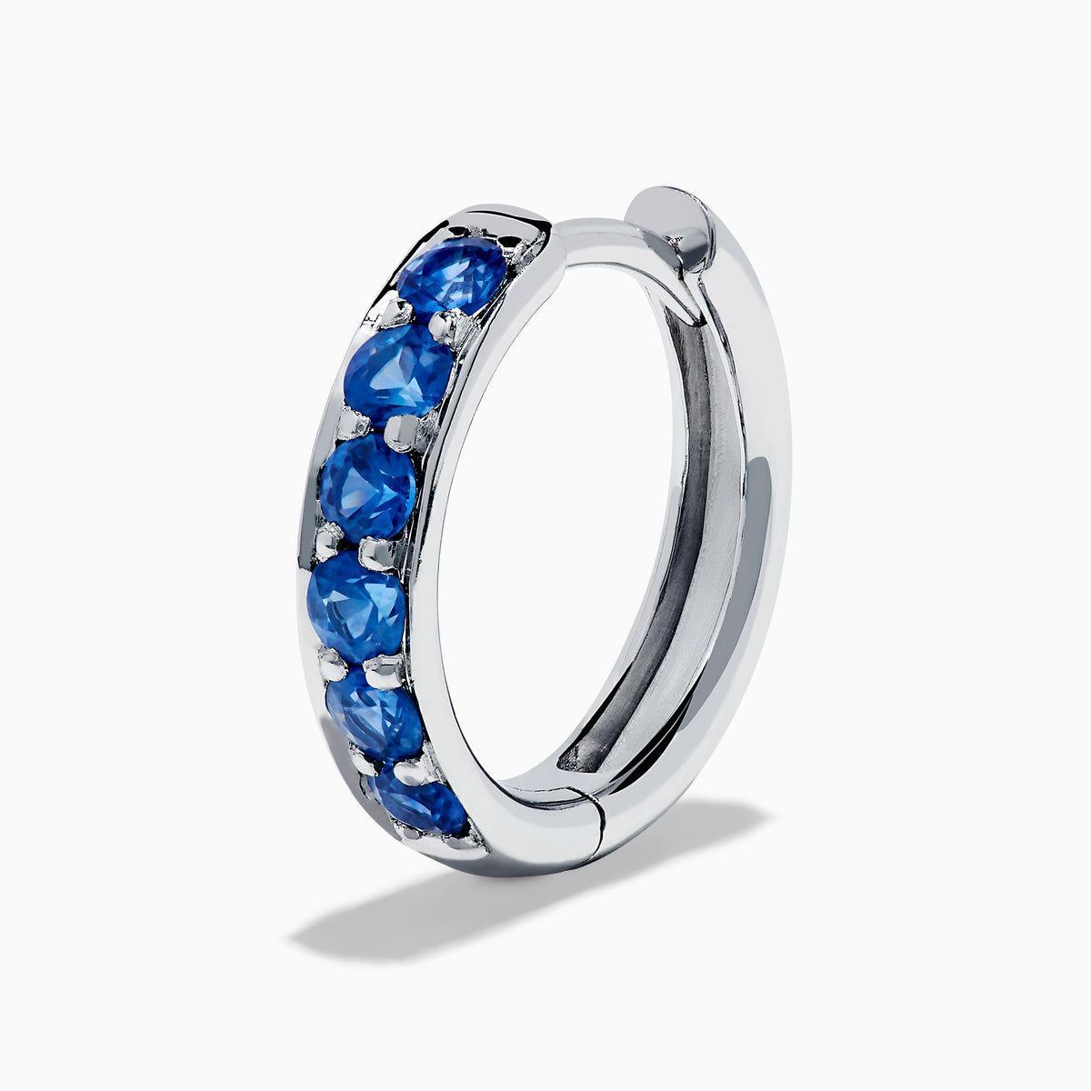 The Royale Bleu 14K White Gold Sapphire Huggie Earrings feature a row of round blue sapphires and are displayed against a white background.