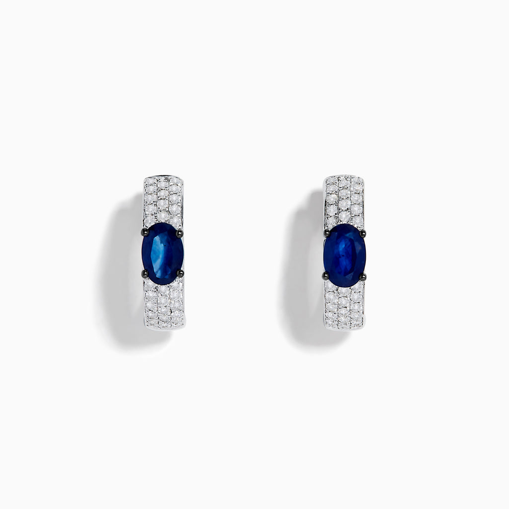 The Royal Bleu 14K White Gold Sapphire and Diamond Huggie Earrings showcase oval sapphire centers surrounded by rows of sparkling diamonds, displayed against a plain white background.