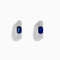 The Royal Bleu 14K White Gold Sapphire and Diamond Huggie Earrings showcase oval sapphire centers surrounded by rows of sparkling diamonds, displayed against a plain white background.