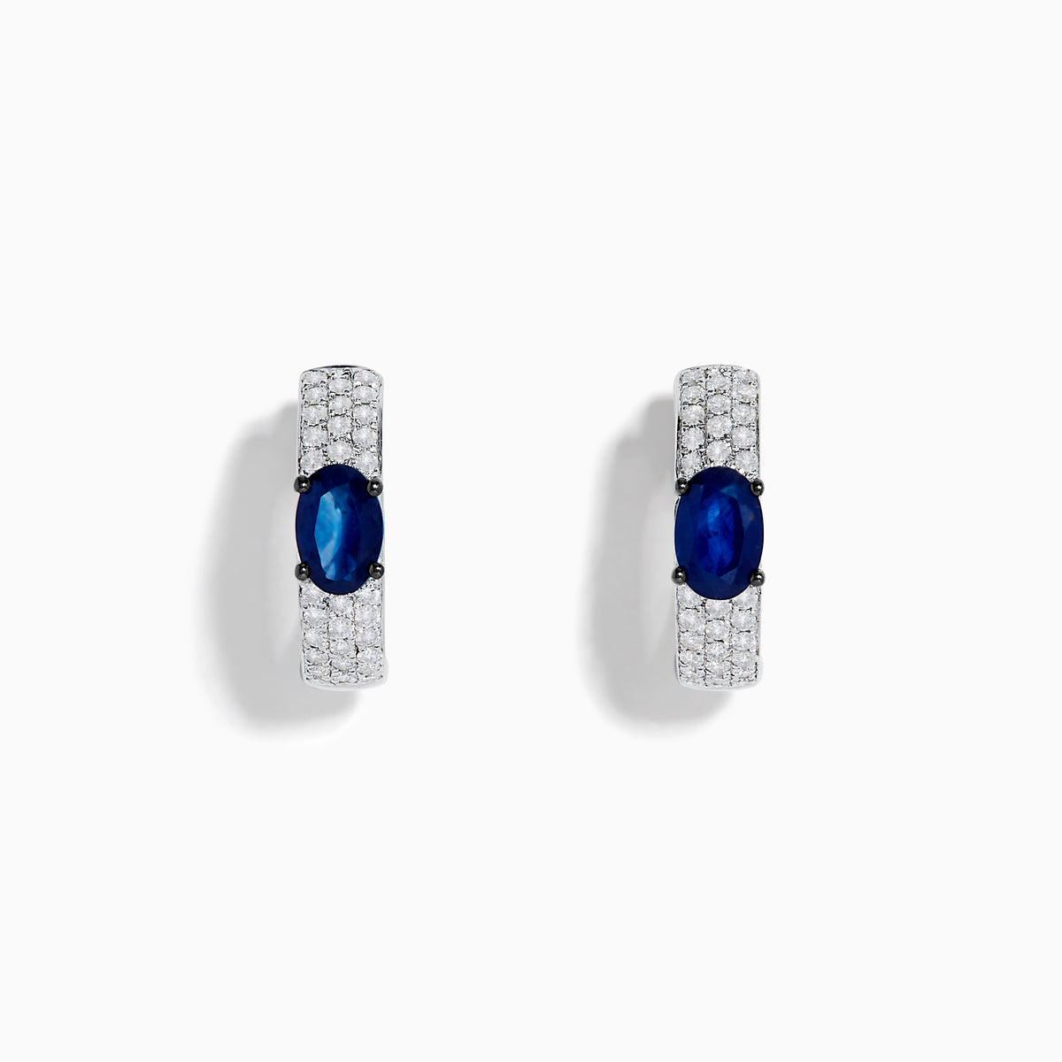 The Royal Bleu 14K White Gold Sapphire and Diamond Huggie Earrings showcase oval sapphire centers surrounded by rows of sparkling diamonds, displayed against a plain white background.