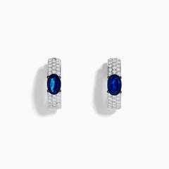 The Royal Bleu 14K White Gold Sapphire and Diamond Huggie Earrings showcase oval sapphire centers surrounded by rows of sparkling diamonds, displayed against a plain white background.