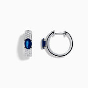The Royal Bleu 14K White Gold Sapphire and Diamond Huggie Earrings showcase oval sapphire centers surrounded by rows of sparkling diamonds, displayed against a plain white background.