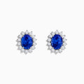 The Nahla Siri 14K White Gold Tanzanite and Diamond Earrings feature oval tanzanite stones surrounded by a halo of sparkling diamonds, elegantly set in white gold and displayed on a white background.