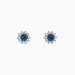Bella Bleu 14K White Gold Blue and White Diamond Earrings, 1.20 TCW, feature a central round blue stone encircled by sparkling white diamonds in a flower-inspired design, displayed on a white background.