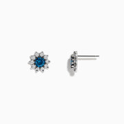 Bella Bleu 14K White Gold Blue and White Diamond Earrings, 1.20 TCW, feature a central round blue stone encircled by sparkling white diamonds in a flower-inspired design, displayed on a white background.