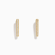 A pair of D'Oro 14K Yellow Gold Diamond Triangle Huggie Earrings are shown on a plain white background, each featuring a row of sparkling diamonds.