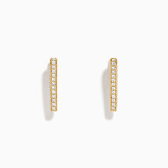 A pair of D'Oro 14K Yellow Gold Diamond Triangle Huggie Earrings are shown on a plain white background, each featuring a row of sparkling diamonds.