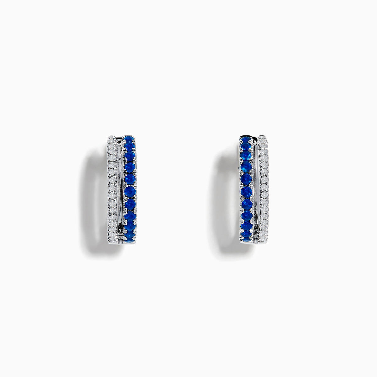 The Royal Bleu 14K White Gold Blue Sapphire and Diamond Huggie Earrings feature a row of blue sapphires bordered by sparkling diamonds on each hoop, shown against a white background.