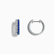 The Royal Bleu 14K White Gold Blue Sapphire and Diamond Huggie Earrings feature a row of blue sapphires bordered by sparkling diamonds on each hoop, shown against a white background.